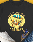 This semi-fitted black womens t-shirt features a vintage design with the quote I Really Enjoy Those Dog Days. A lounging dog under an umbrella adds a touch of whimsy for any dog lover. Designed by Dog Gang.