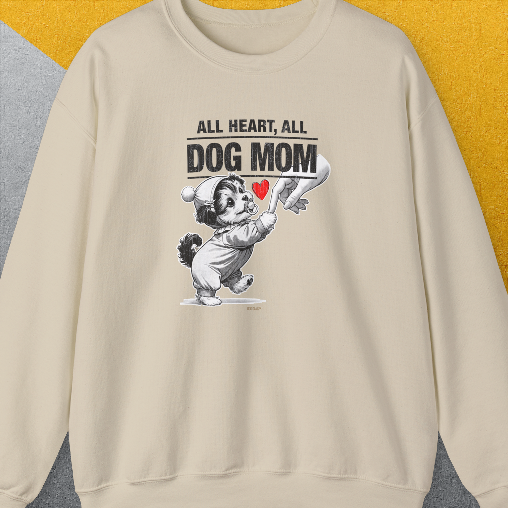 The Dog Mom Series, Volume 9 sweatshirt is a beige crewneck emblazoned with a delightful illustration of a dog dressed in a baby outfit, holding a woman's hand. Prominently displayed above the image is the phrase All Heart, All Dog Mom, accentuated with a vibrant red heart. Shirtdesign by Dog Gang ensures this piece stands out with its commitment to quality and design, using ethically grown cotton and OEKO-TEX-certified dyes for an eco-friendly and stylish choice.