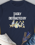 The navy Easily Distracted By Dogs Series, Volume 1 womens t-shirt is made from soft ringspun cotton, perfect for dog lovers. It features the text in white and gold, creatively formed by dog illustrations like a Dalmatian, a Golden Retriever, a Pug, a Poodle, Dachshund, French Bulldog, Chihuahua, Husky and more. Designed by Dog Gang.