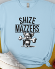 The light blue t-shirt displays a funny cartoon dog holding an oversized bone in its mouth, preventing it from speaking properly. The text reads "SHIZE MAZZERS". Perfect for any dog lover. Designed by Dog Gang.