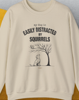 The My Dog Is Easily Distracted By - Volume 1: Squirrels unisex sweatshirt features a funny dog design with playful text and a curious dog under a tree. Designed by Dog Gang.