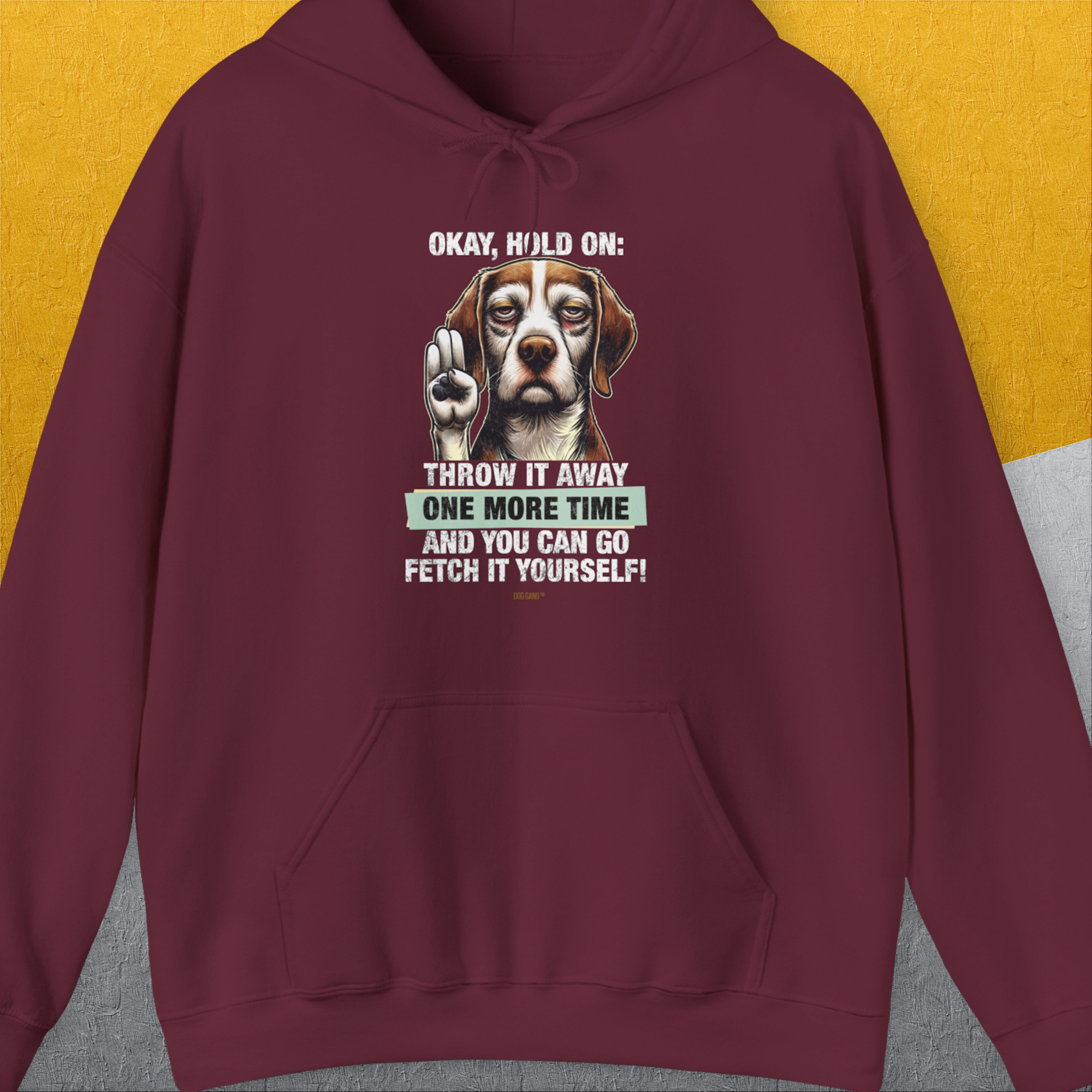 The Go Fetch It Yourself Series, Volume 3, Unisex Hoodie features a playful dog graphic with Throw it away one more time and you can go fetch it yourself! on maroon fabric. Perfect for the funny dog person. Designed by Dog Gang.