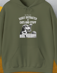 This olive green unisex hoodie showcases the playful theme My Dog Is Easily Distracted By - Volume 2: Cats And Stuff. The design prominently features a white graphic illustration of a dog intently watching a cat over a fence, accompanied by text. Crafted from ethically grown US cotton, its both comfortable and stylish. Shirtdesign by Dog Gang adds an authentic touch to this uniquely charming piece.
