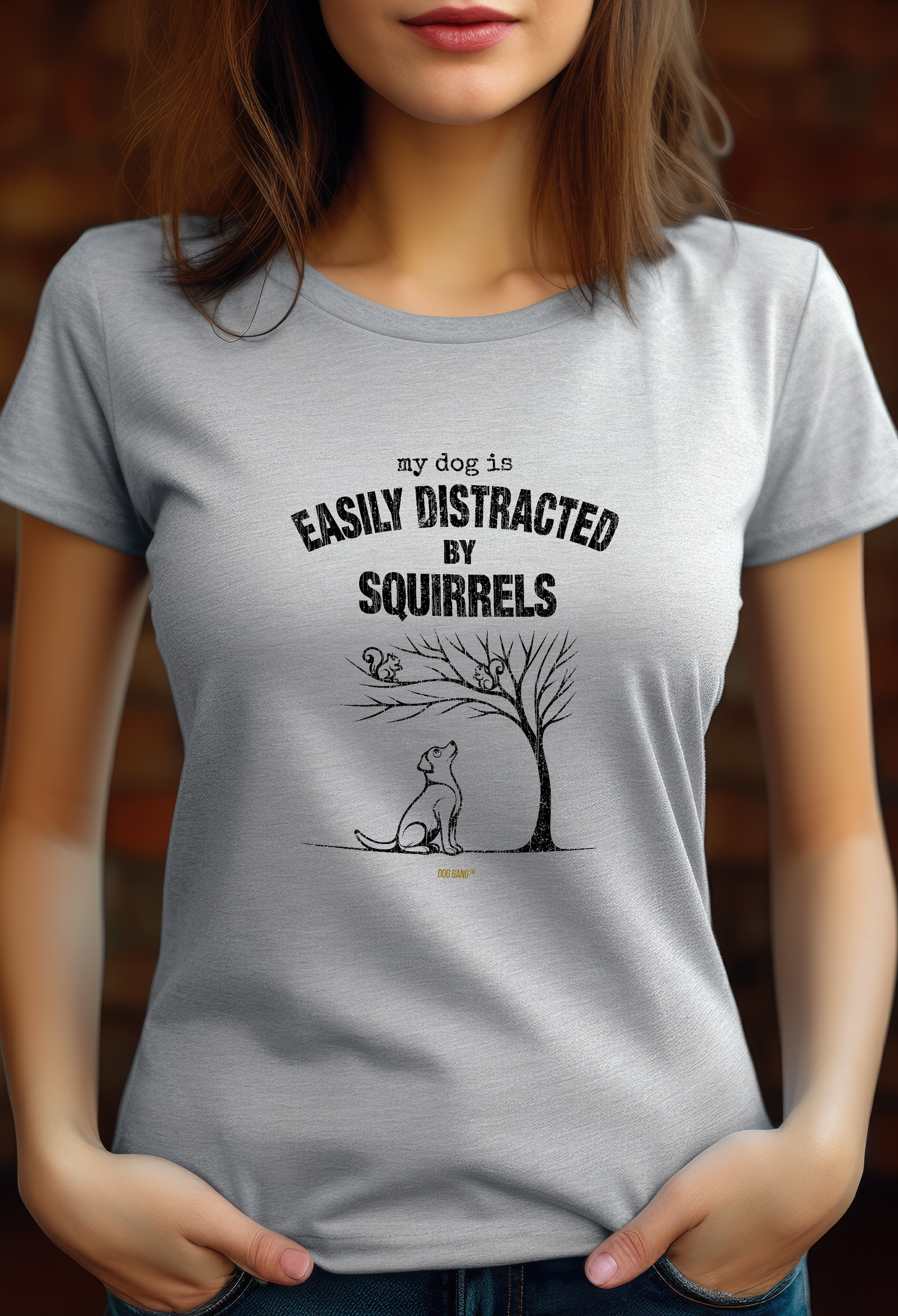 A person wears a gray Dog Gang t-shirt with a graphic of a dog looking at a squirrel in a tree. Above the graphic is the text "My dog ​​is easily distracted by squirrels."