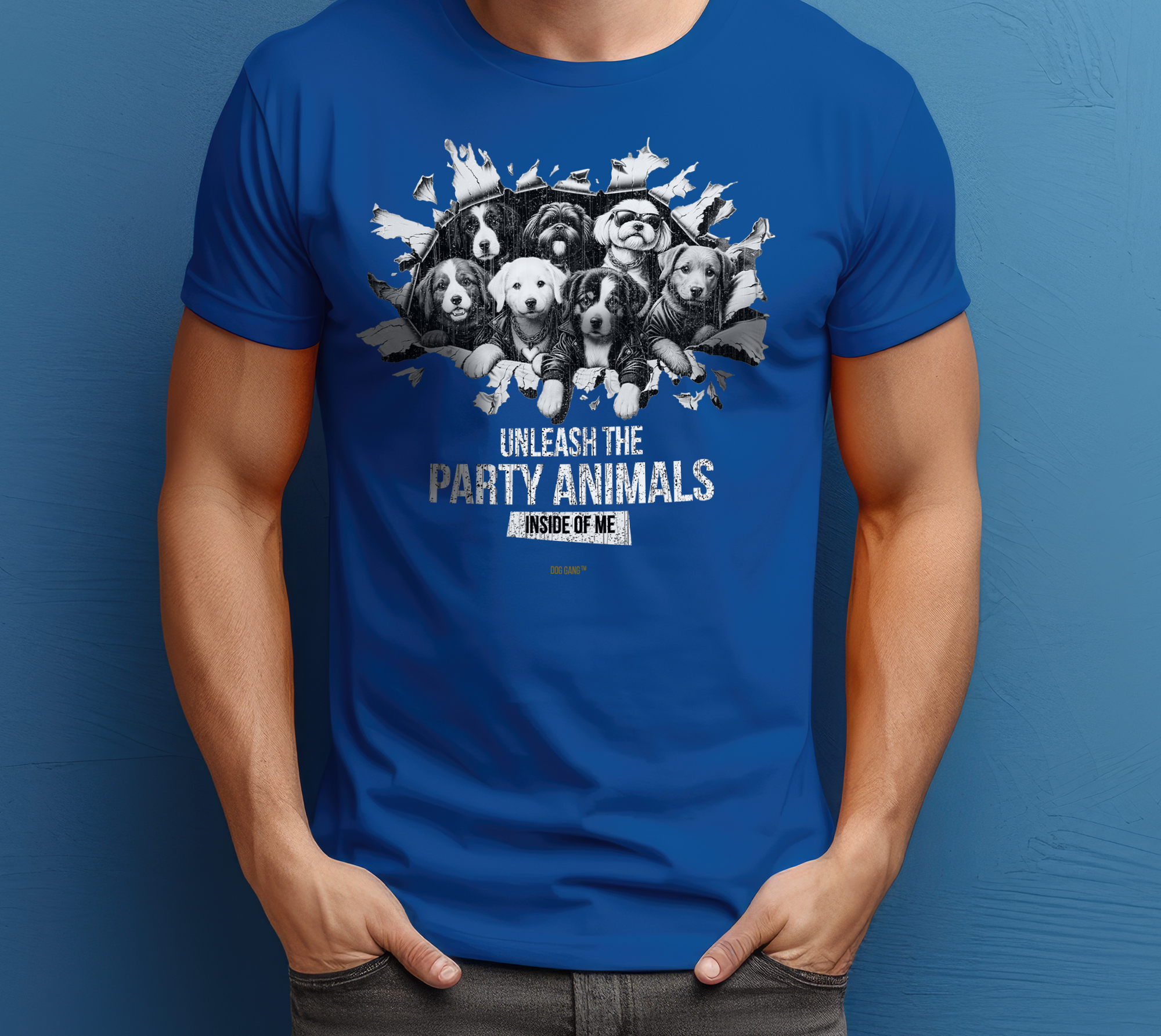 The man is wearing a blue T-shirt from the design label DOG GANG with a pattern of cartoon dogs breaking through the fabric. The text reads: "Unleash the party animal inside of me" The man is standing in front of a blue wall with his hands in his pockets.