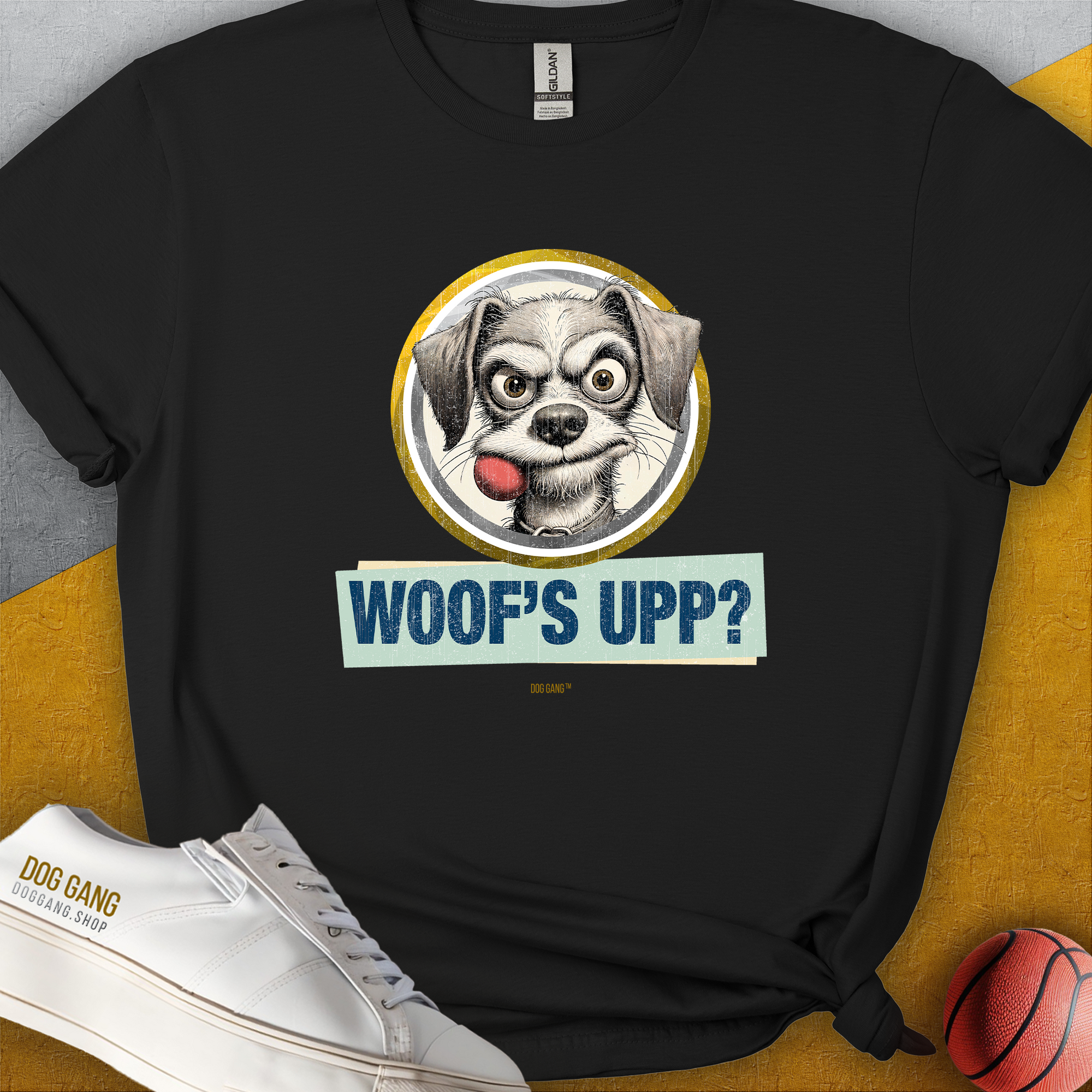 The Woofs Upp? Volume 1 T-shirt features a cartoon dog with a fetch ball in his mouth and the phrase &quot;WOOFS UPP?&quot; Perfect for any dog lover, its a fun and playful design. Designed by Dog Gang.